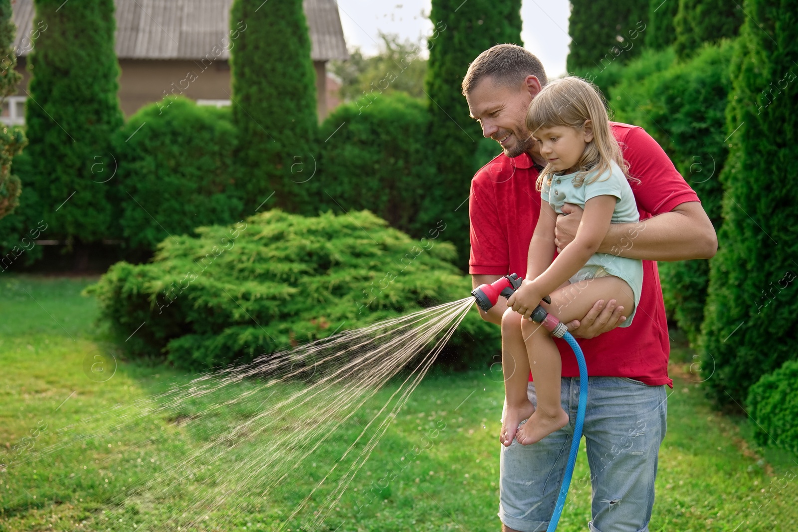 Photo of Father and his daughter watering lawn with hose in backyard