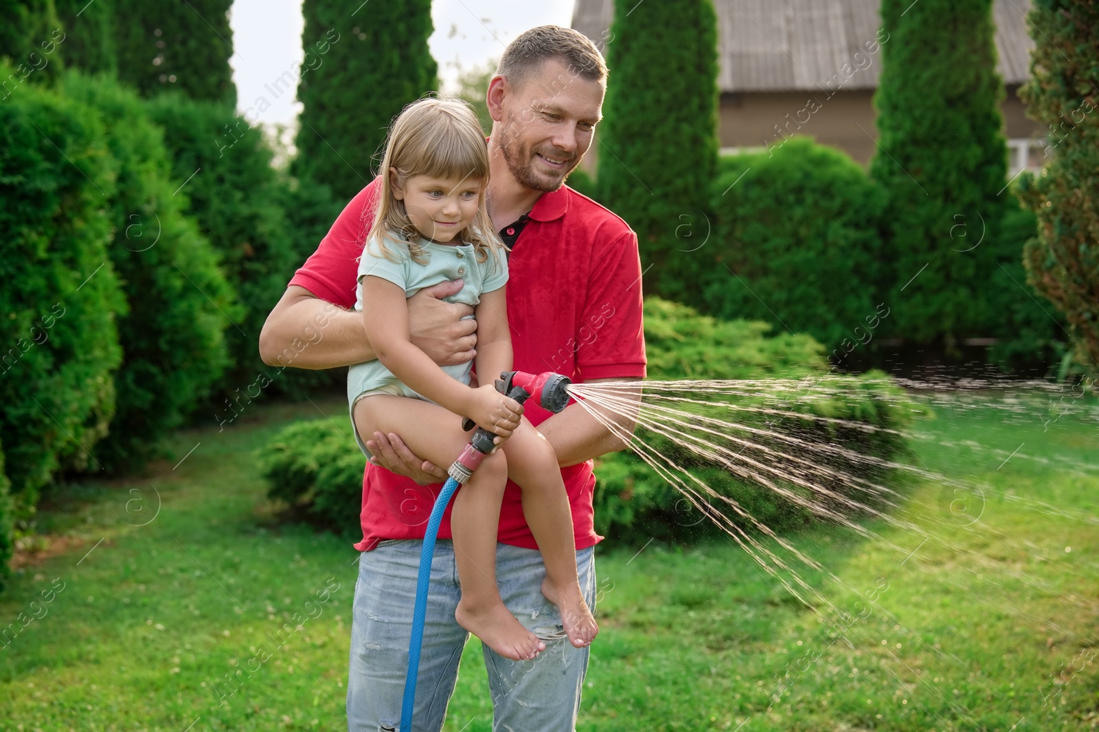 Photo of Father and his daughter watering lawn with hose in backyard