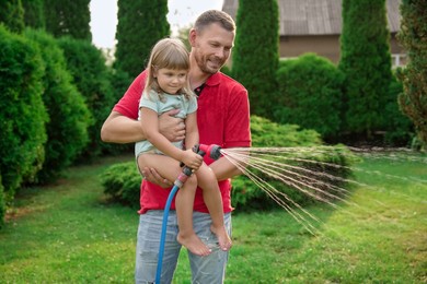 Photo of Father and his daughter watering lawn with hose in backyard