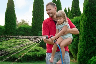 Father and his daughter watering lawn with hose in backyard