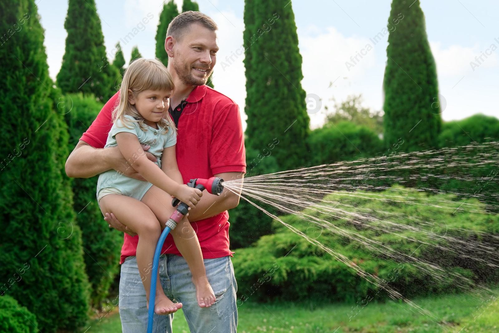 Photo of Father and his daughter watering lawn with hose in backyard