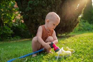 Photo of Little boy with hose on green lawn in backyard