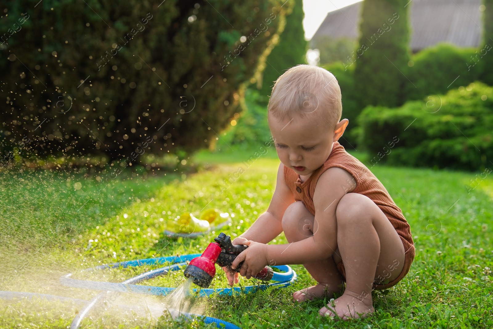 Photo of Little boy with hose on green lawn in backyard