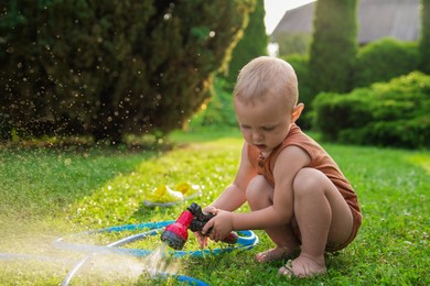 Little boy with hose on green lawn in backyard