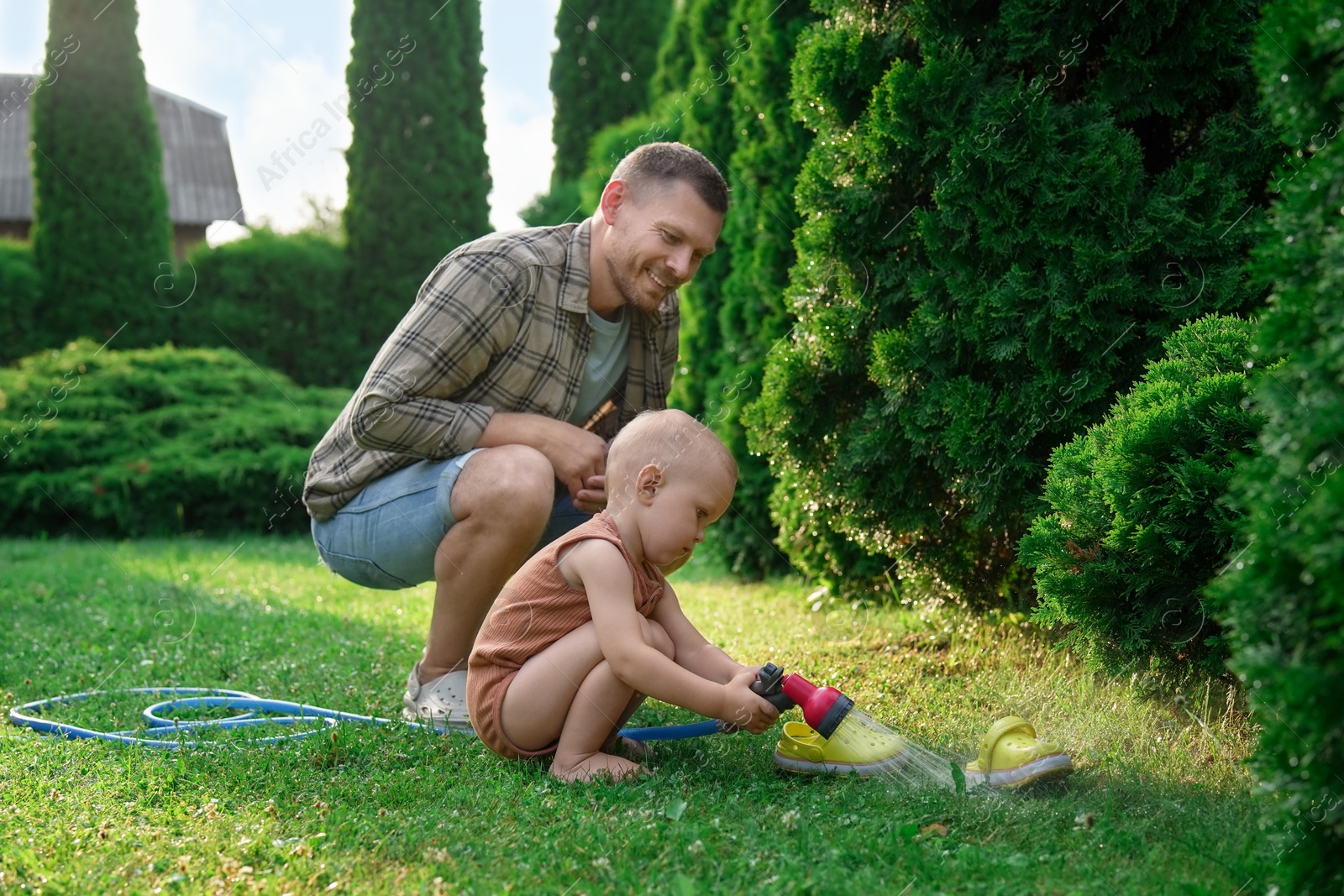 Photo of Father and his son watering lawn with hose in backyard