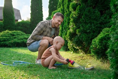 Father and his son watering lawn with hose in backyard