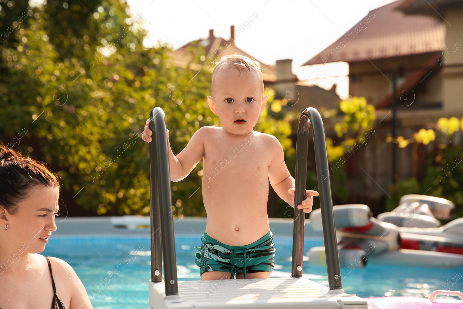 Photo of Little boy getting out of swimming pool by ladder outdoors