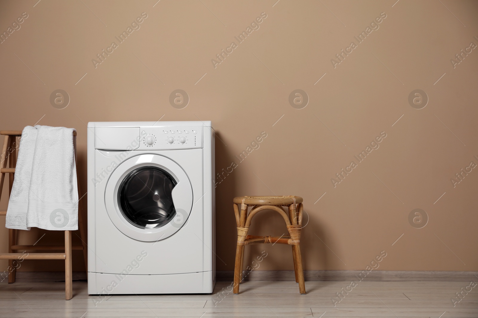 Photo of Washing machine, towel on decorative folding ladder and chair near beige wall indoors, space for text