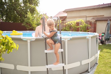 Photo of Little girl getting out of swimming pool by ladder outdoors