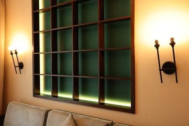 Empty illuminated wooden shelving unit and lamps on beige wall in hotel room