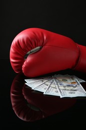 Photo of Red boxing glove and dollar banknotes on black mirror surface