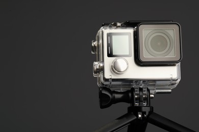 Modern action camera and tripod on grey background, closeup. Space for text