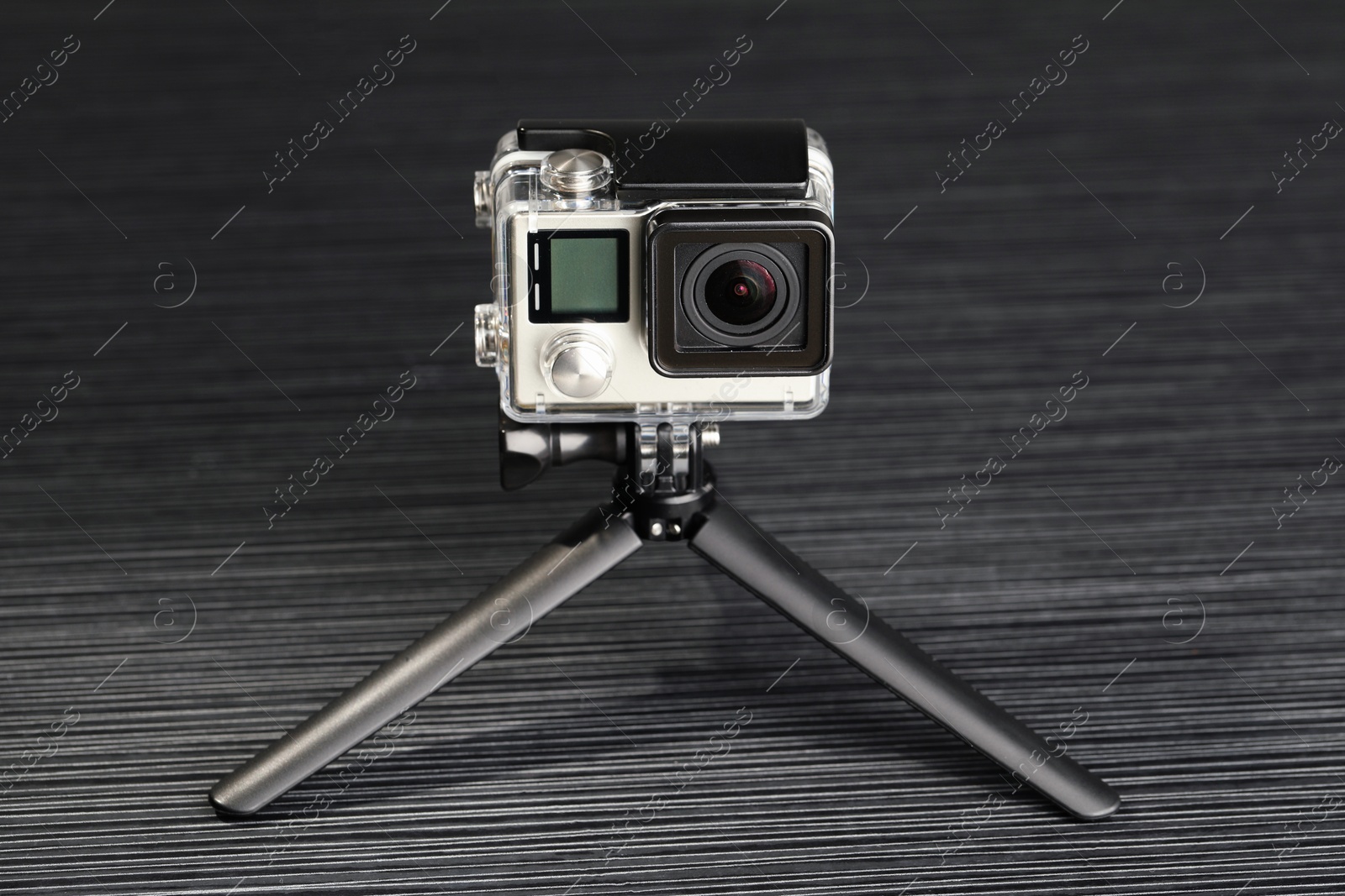 Photo of Modern action camera and tripod on grey wooden table