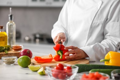 Professional chef cutting pepper at table in kitchen, closeup