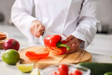 Professional chef cutting pepper at table in kitchen, closeup