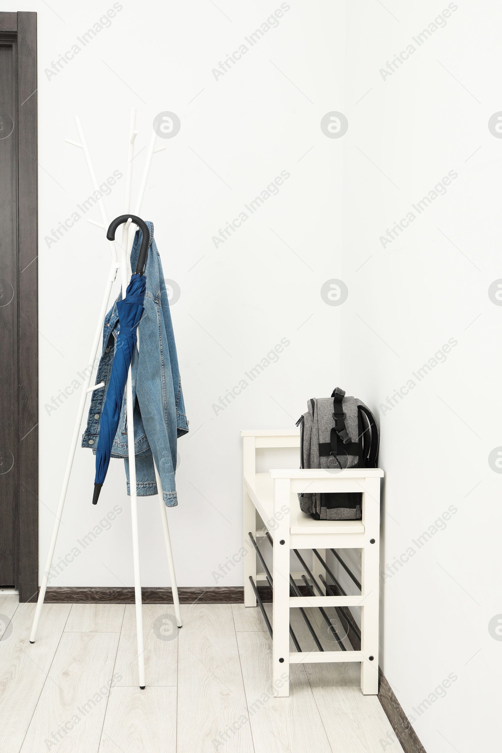 Photo of Blue umbrella and denim jacket on clothing rack near shoe storage bench with backpack in hallway