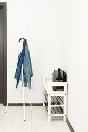 Photo of Blue umbrella and denim jacket on clothing rack near shoe storage bench with backpack in hallway