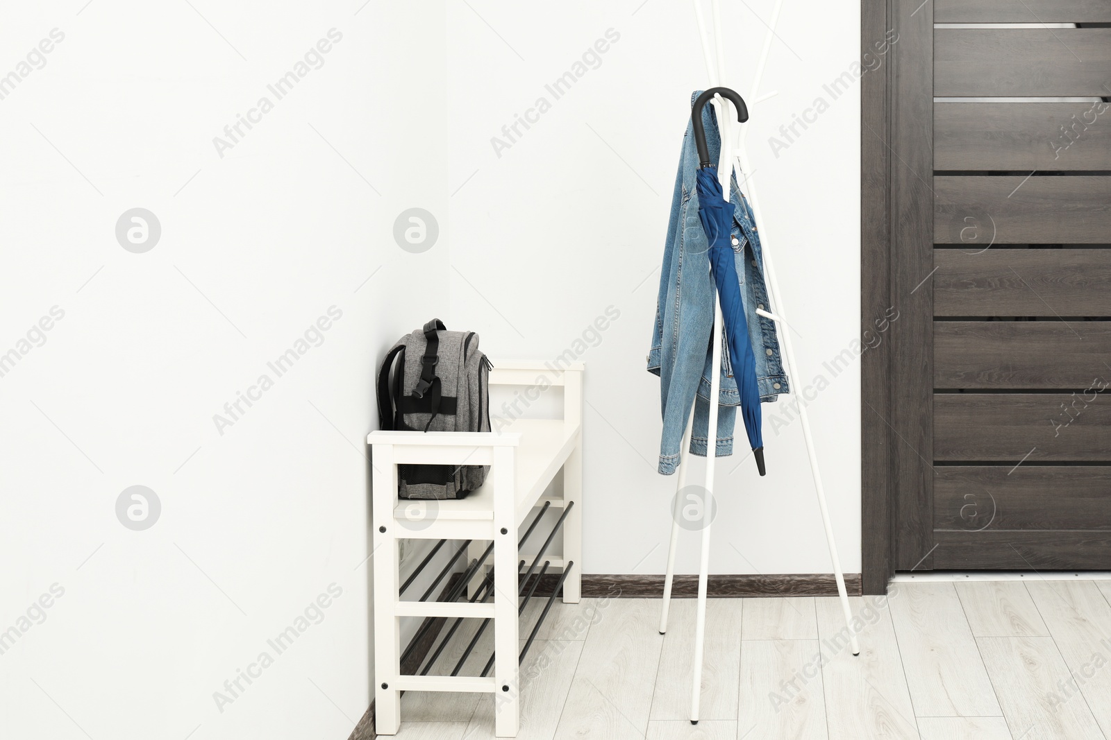 Photo of Blue umbrella and denim jacket on clothing rack near shoe storage bench with backpack in hallway