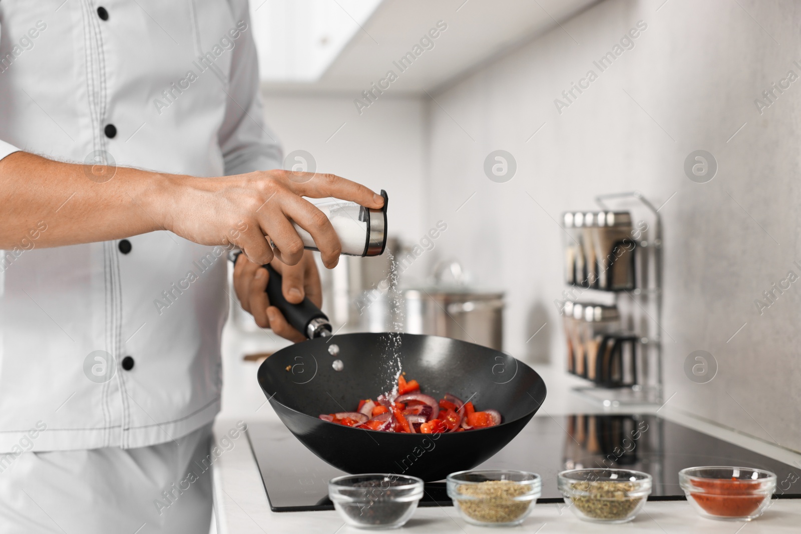 Photo of Professional chef adding salt into frying pan in kitchen, closeup