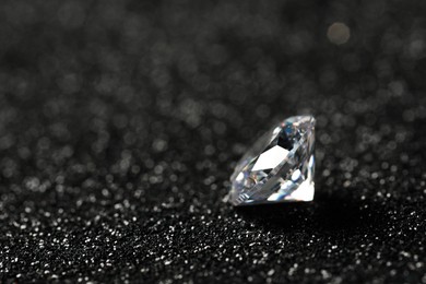 Beautiful dazzling diamond on dark shiny background, closeup. Space for text