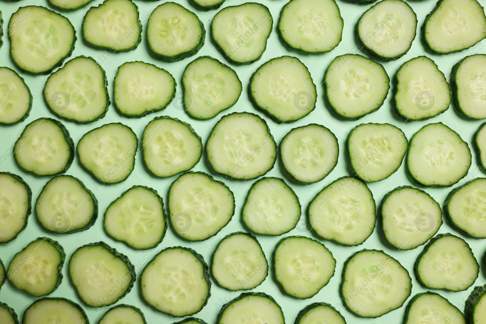 Photo of Slices of fresh cucumbers on turquoise background, flat lay