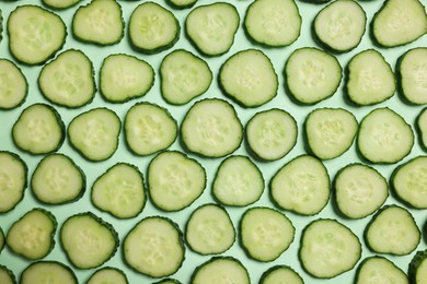 Photo of Slices of fresh cucumbers on turquoise background, flat lay