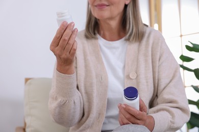 Photo of Senior woman with bottles of pills at home, closeup