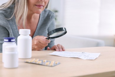 Senior woman with magnifying glass reading medicine instruction at table indoors, closeup