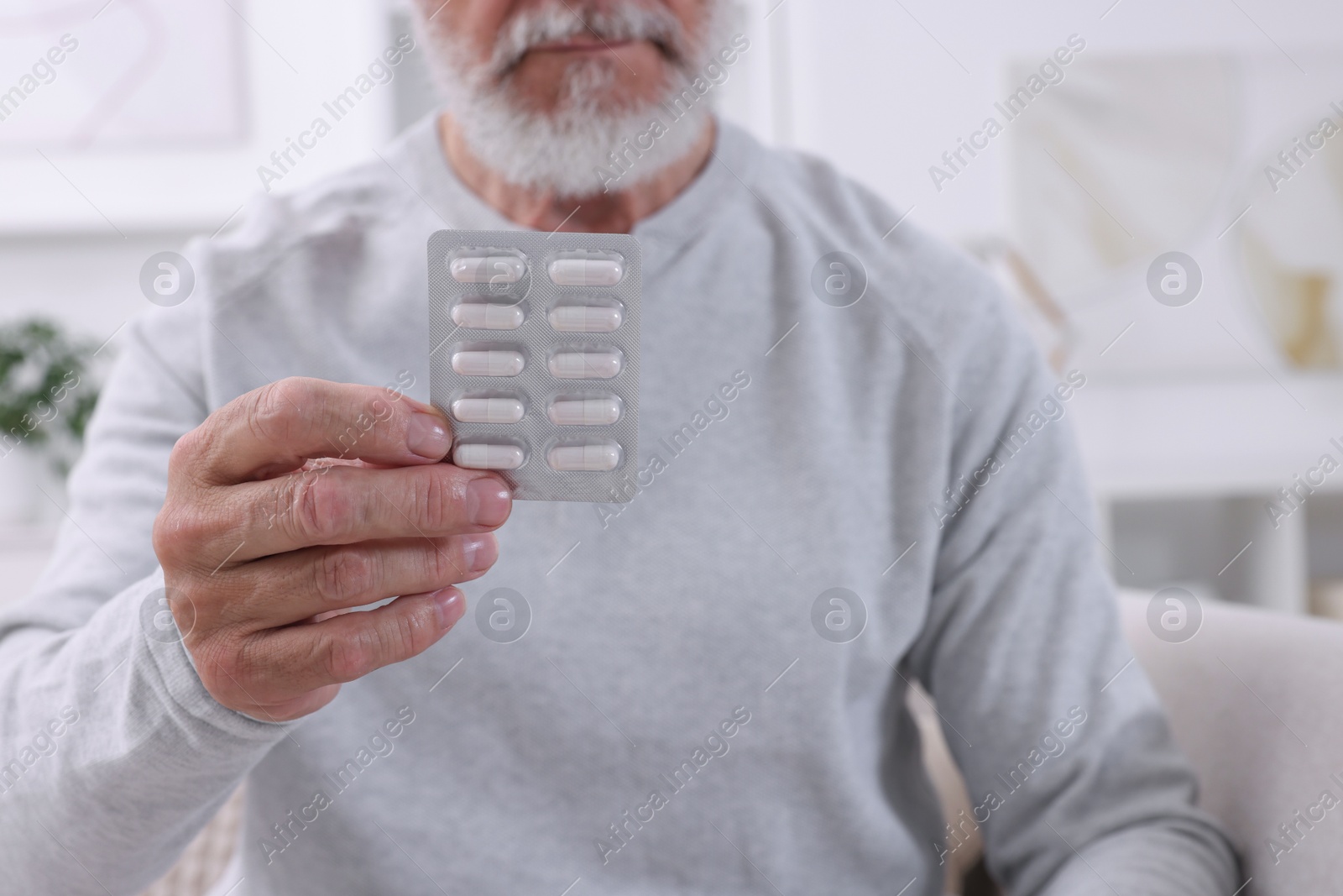 Photo of Senior man holding blister with pills at home, closeup