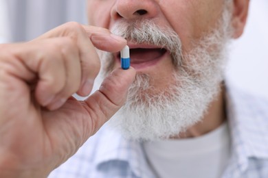 Senior man taking pill at home, closeup