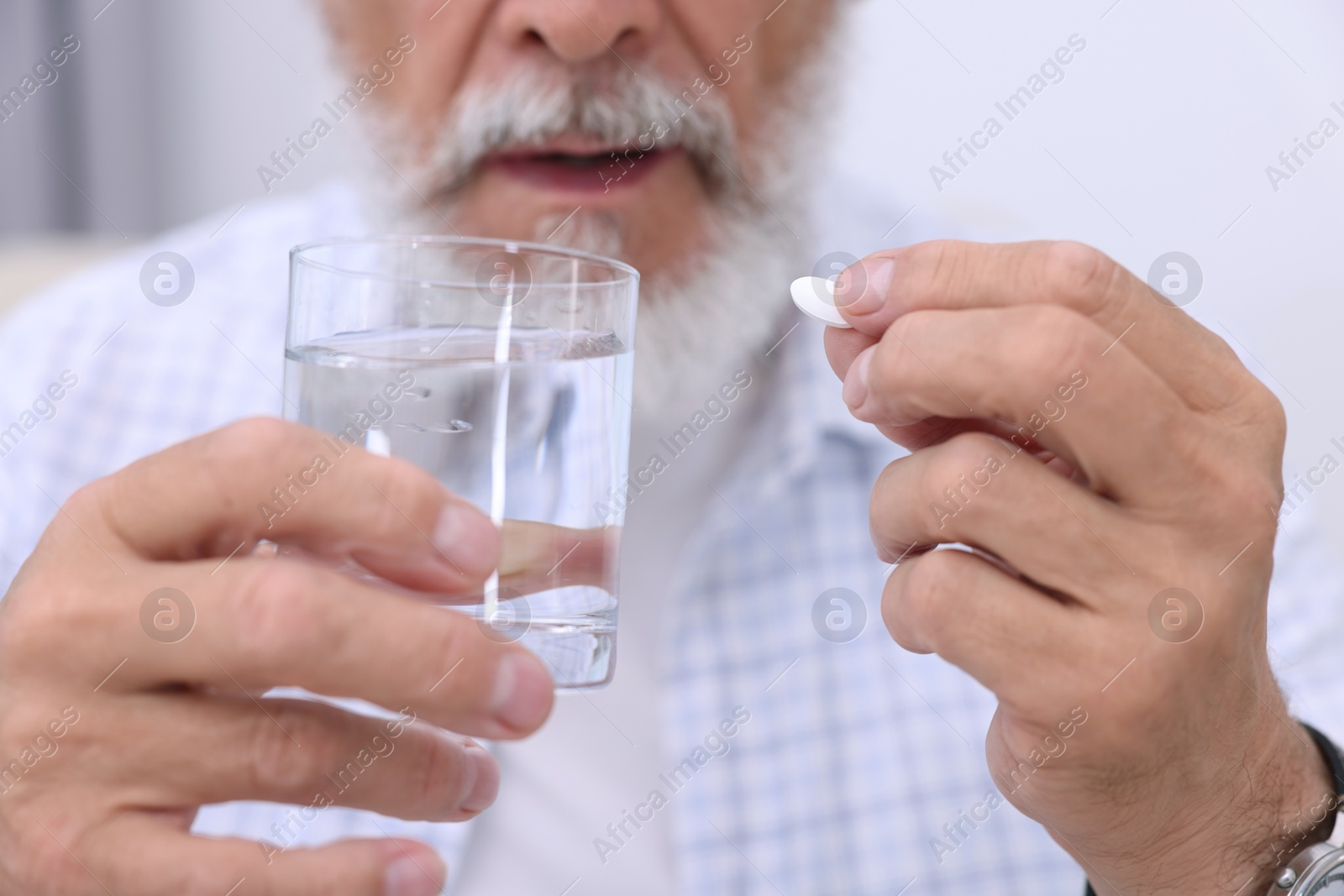 Photo of Senior man with glass of water taking pill at home, closeup