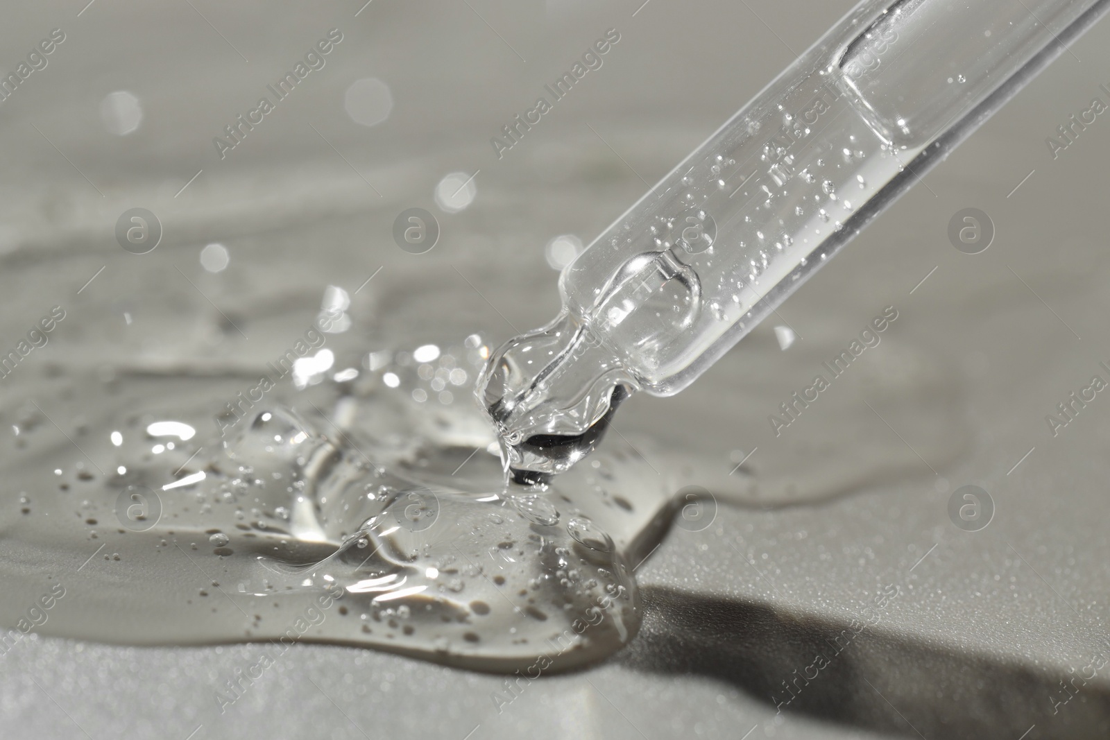 Photo of Dripping cosmetic serum from pipette on grey background, closeup