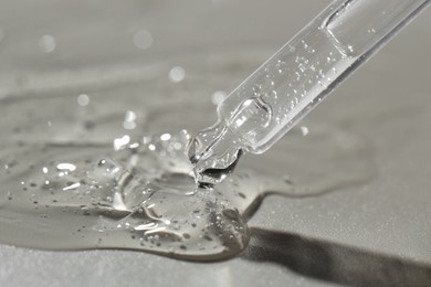 Photo of Dripping cosmetic serum from pipette on grey background, closeup