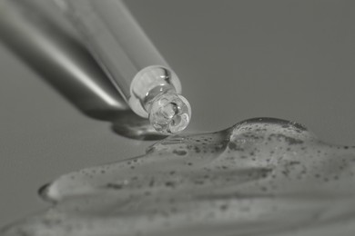 Photo of Dripping cosmetic serum from pipette on grey background, closeup