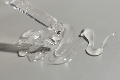 Dripping cosmetic serum from pipette on grey background, closeup