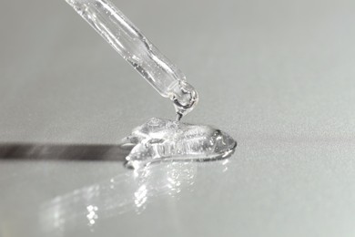 Photo of Dripping cosmetic serum from pipette on grey background, closeup