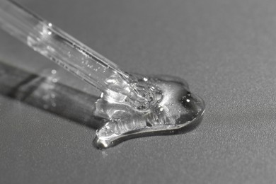 Photo of Dripping cosmetic serum from pipette on grey background, closeup