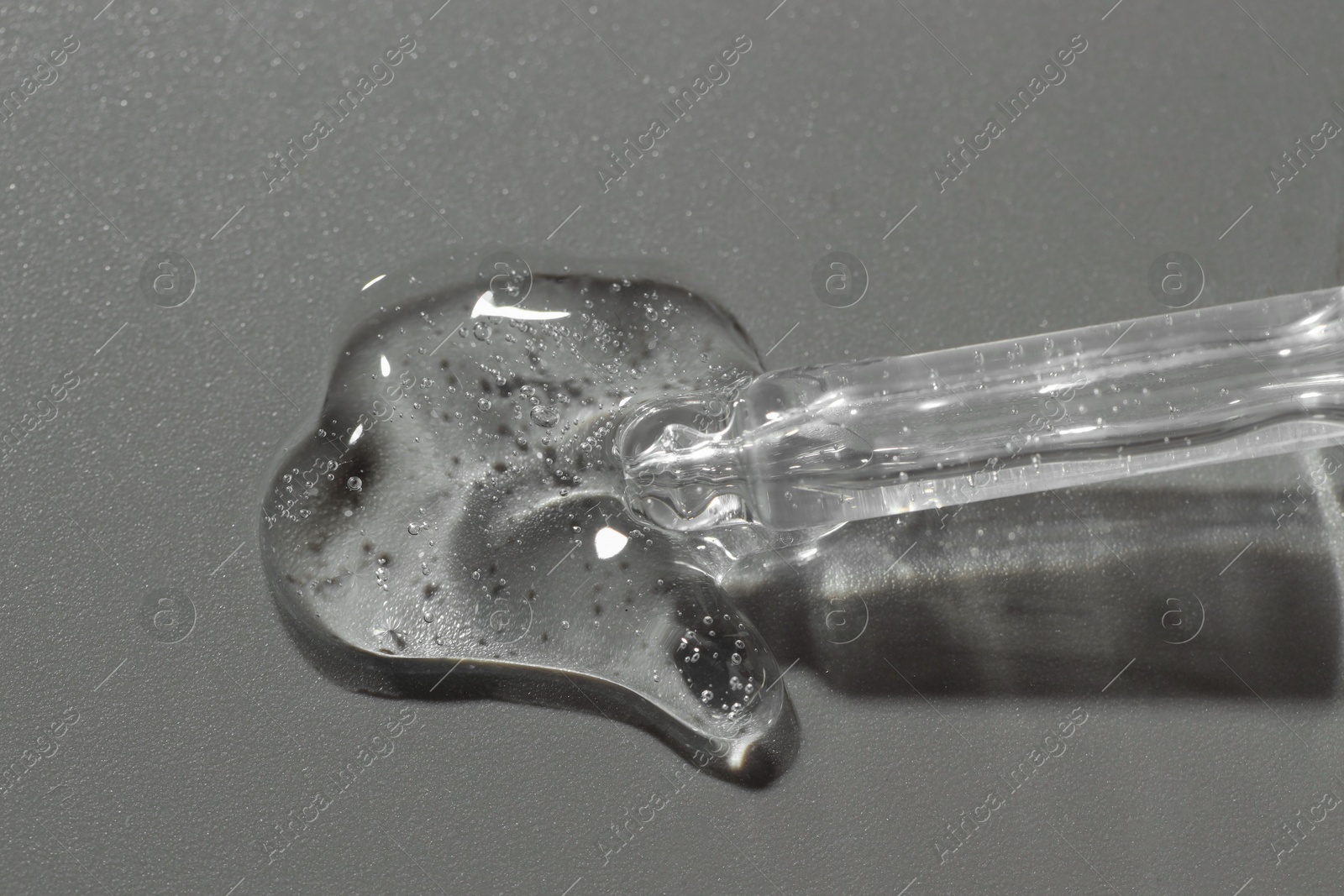 Photo of Dripping cosmetic serum from pipette on grey background, top view