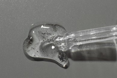 Photo of Dripping cosmetic serum from pipette on grey background, top view