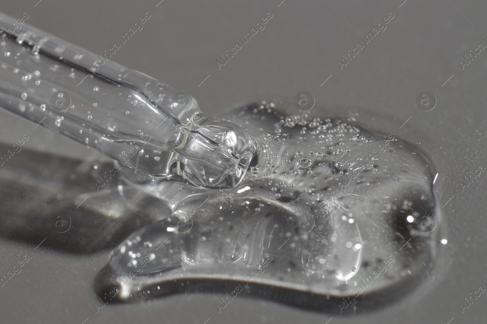 Photo of Dripping cosmetic serum from pipette on grey background, closeup