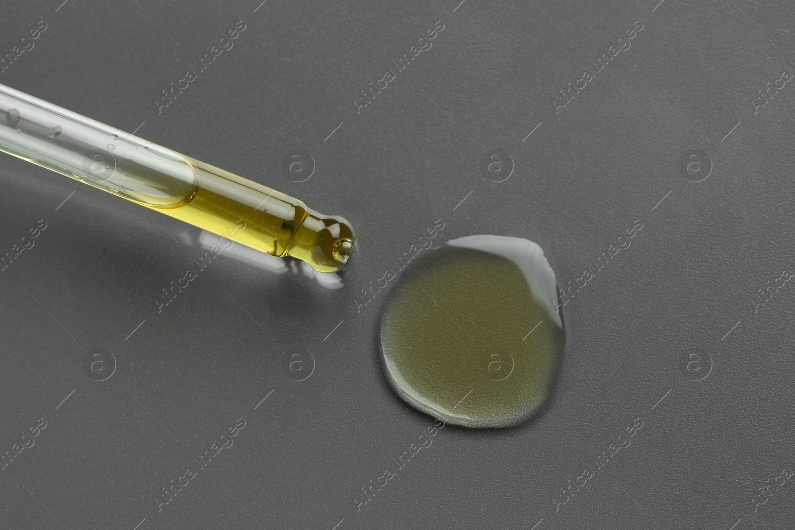 Photo of Dripping essential oil from pipette on grey background, top view