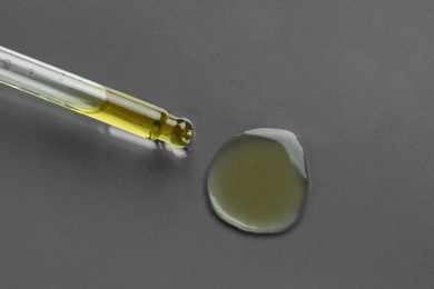 Dripping essential oil from pipette on grey background, top view