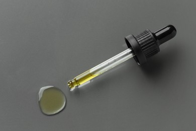 Photo of Dripping essential oil from pipette on grey background, top view