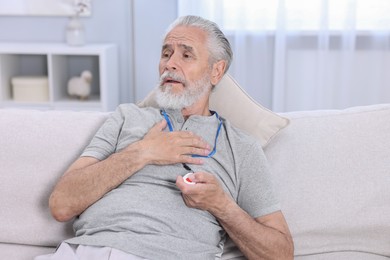 Photo of Senior man suffering from heart pain pressing emergency call button at home