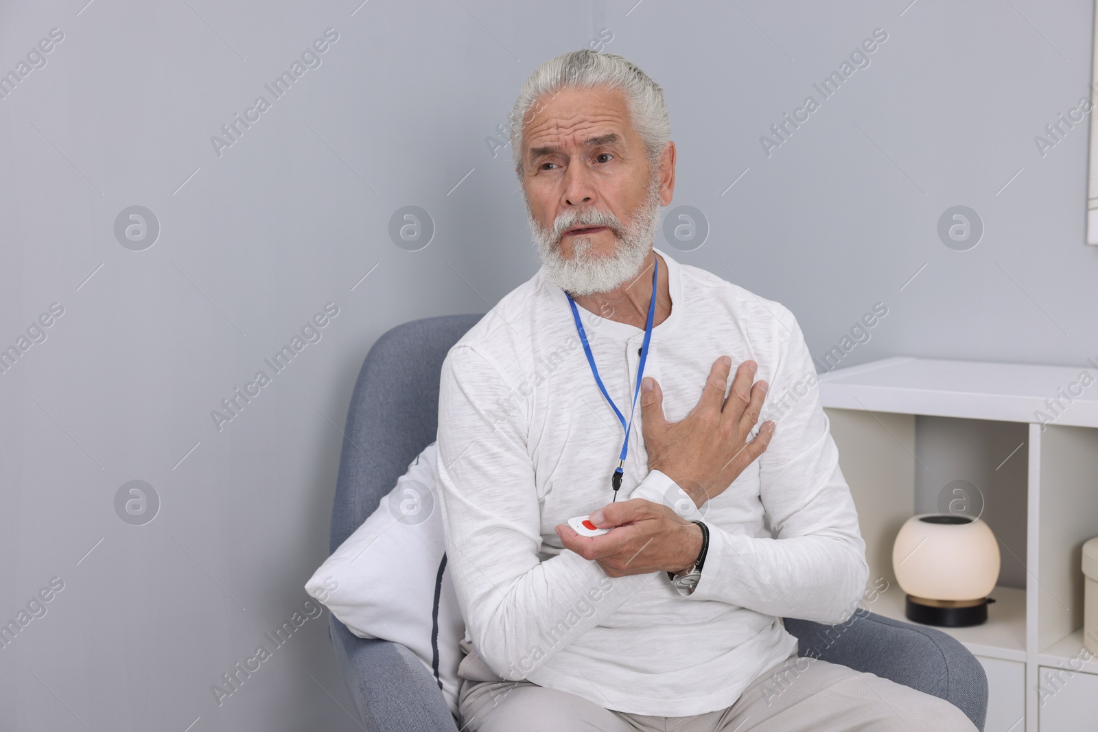 Photo of Senior man suffering from heart pain pressing emergency call button at home