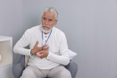 Photo of Senior man suffering from heart pain pressing emergency call button at home, space for text