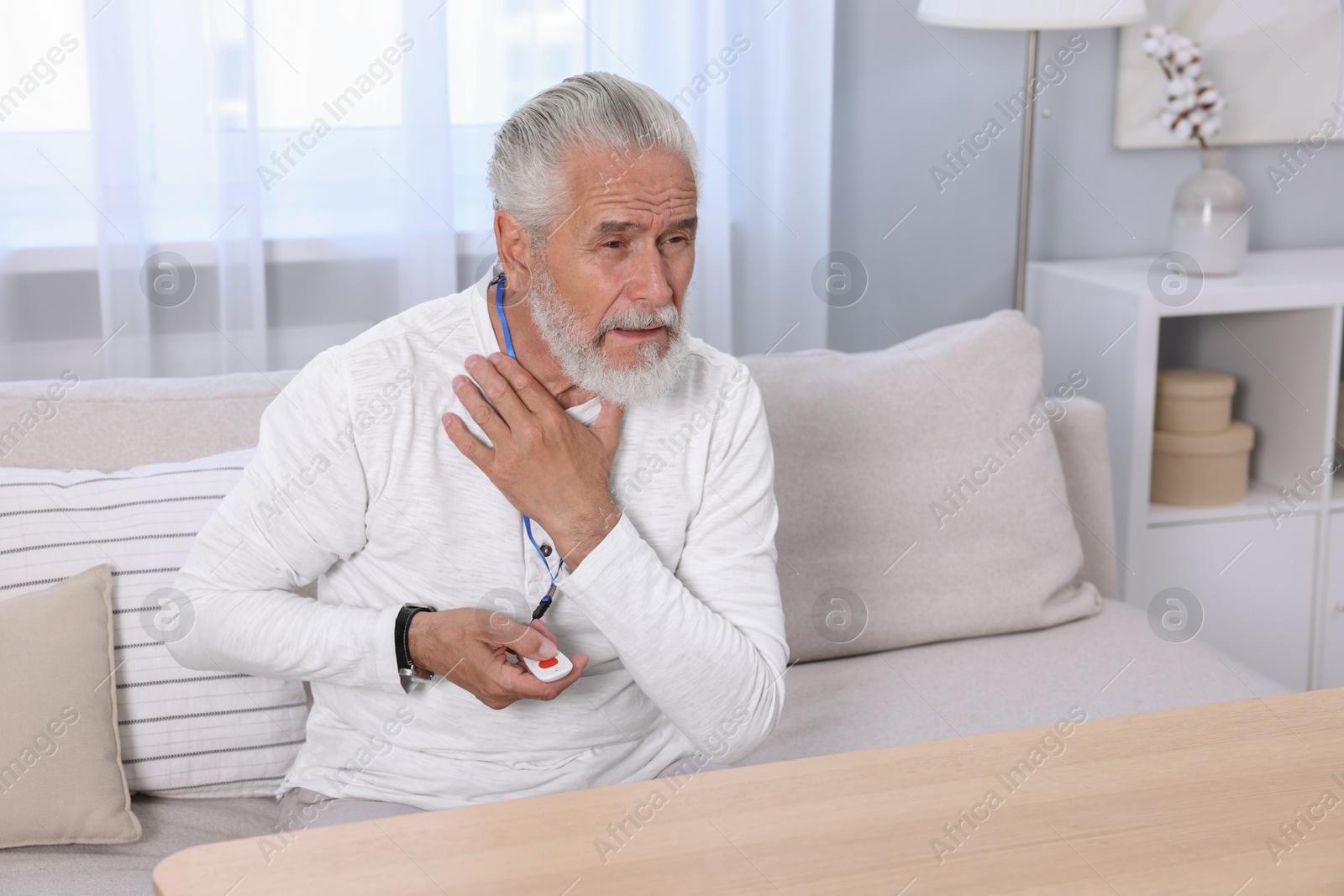 Photo of Senior man suffering from neck pain pressing emergency call button at home