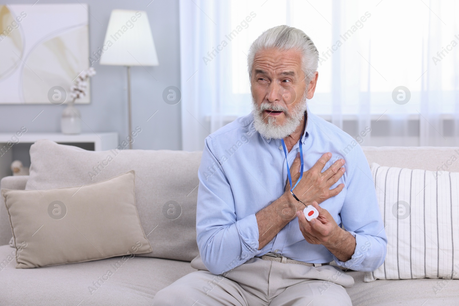 Photo of Senior man suffering from heart pain holding emergency call button at home