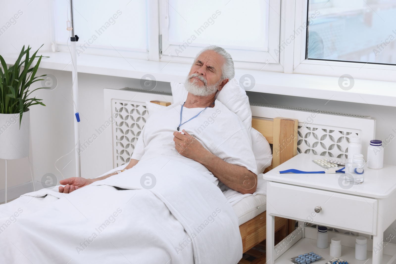 Photo of Senior man with emergency call button on bed in hospital