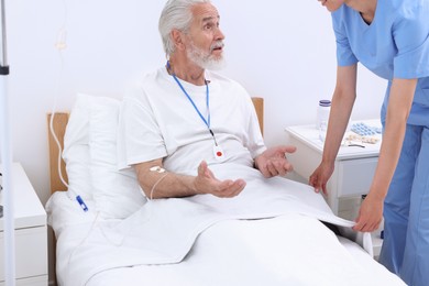 Senior man with emergency call button talking to nurse in hospital